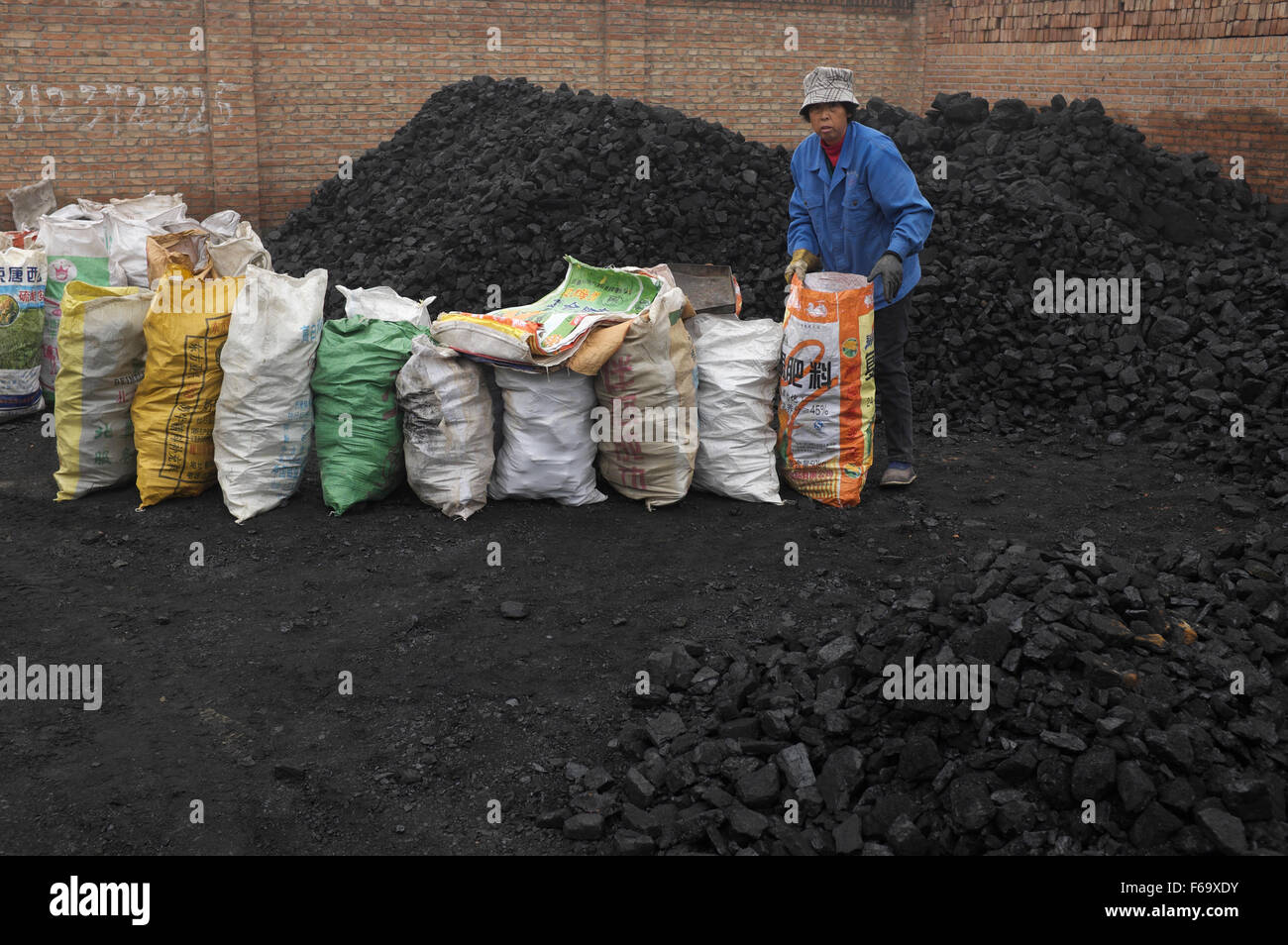A woman bags blocks of coal at a coal store in a village in GuAn, 50km to Beijing, Hebei province, China. Stock Photo