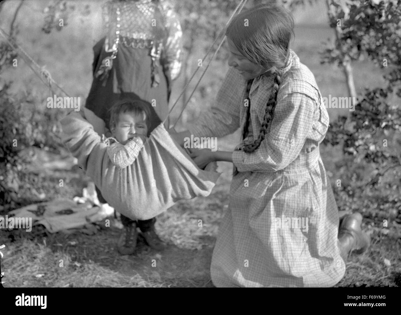 This image captures a Cree girl playing with a child suspended in a ...