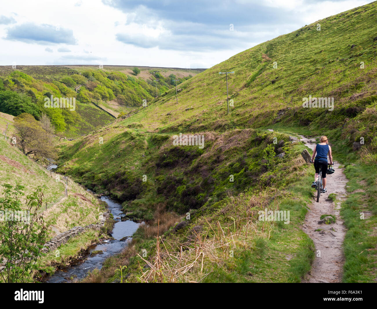 Woman cycling on a bridleway approaching Three Shire Heads in the Peak District, UK Stock Photo