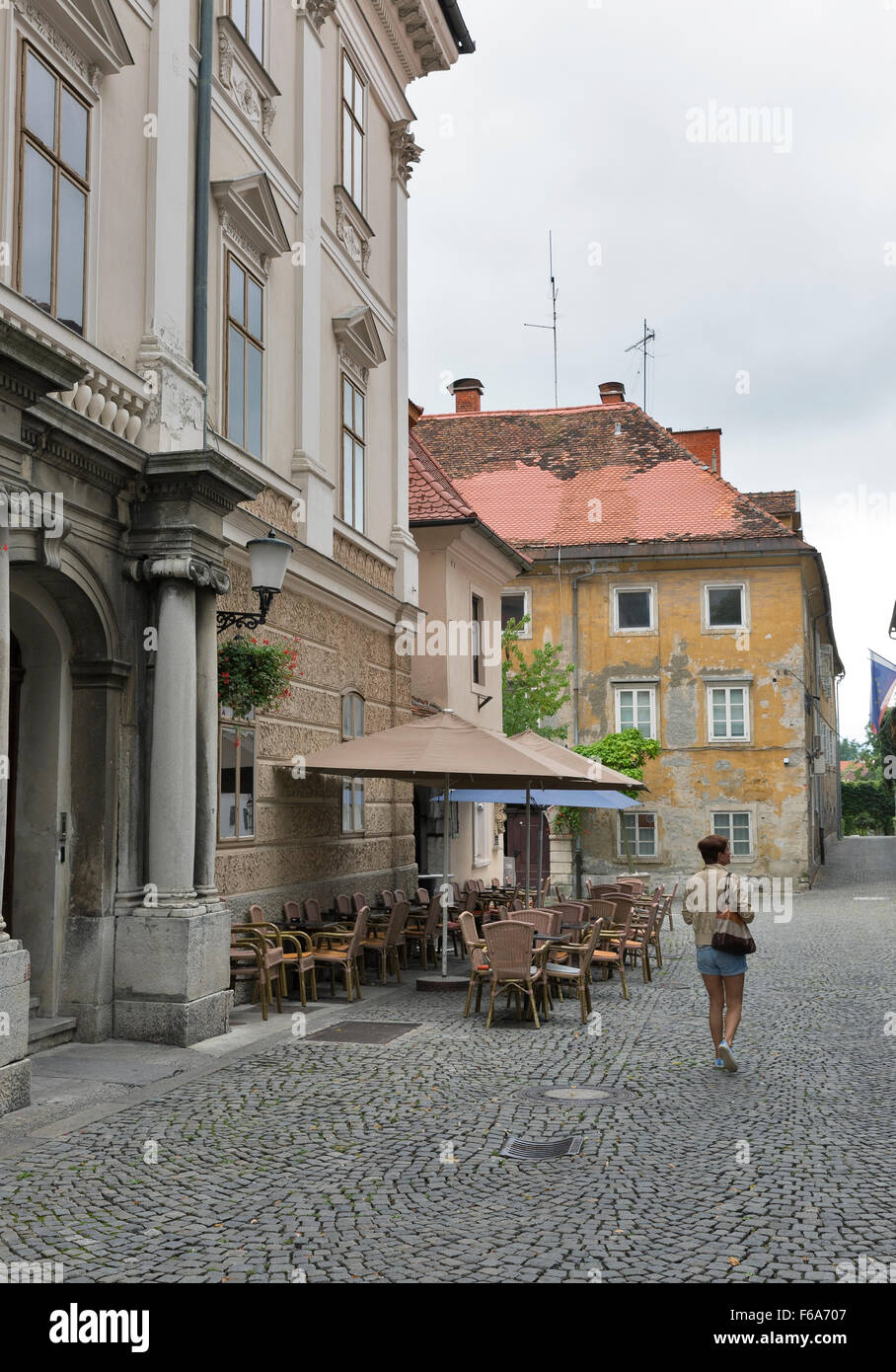 Woman walk along Ljubljana narrow street in front of street cafe. Slovenia. Stock Photo