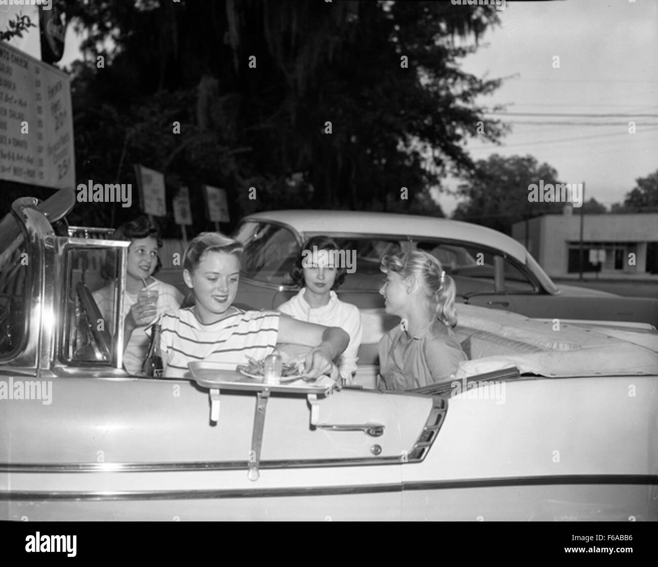 This photograph captures teenagers at a drive-in in Tallahassee, reflecting the 1950s culture of socializing at drive-in theaters and the rise of automobile-based entertainment. The drive-in was a key element of youth culture during the post-WWII era. Stock Photo