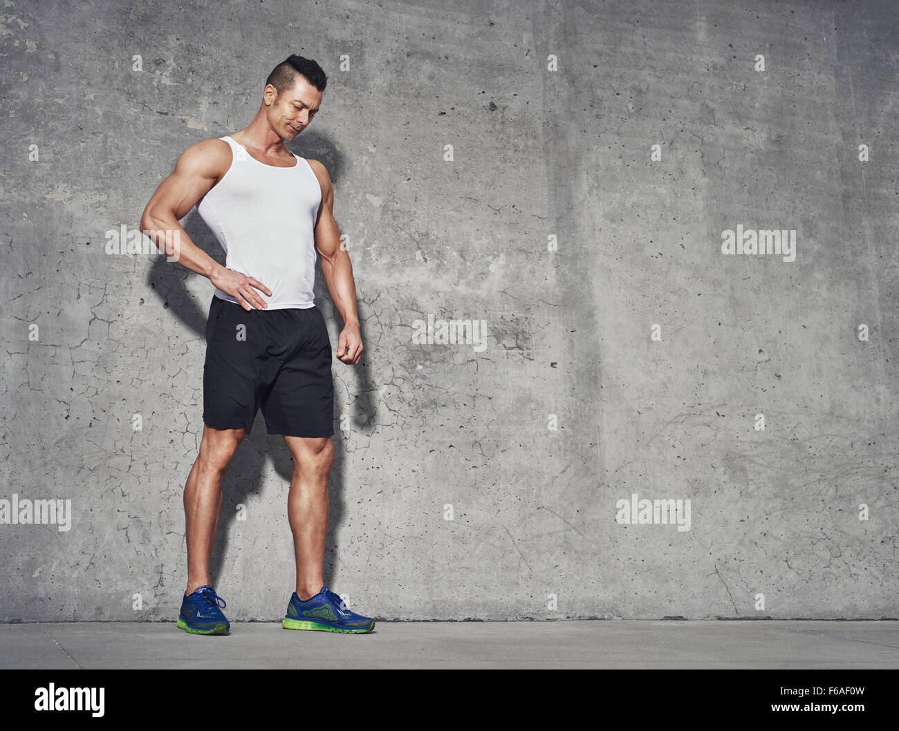 Male fitness model in white tank top relaxing after workout. Grey background with room for text, Copy space Stock Photo