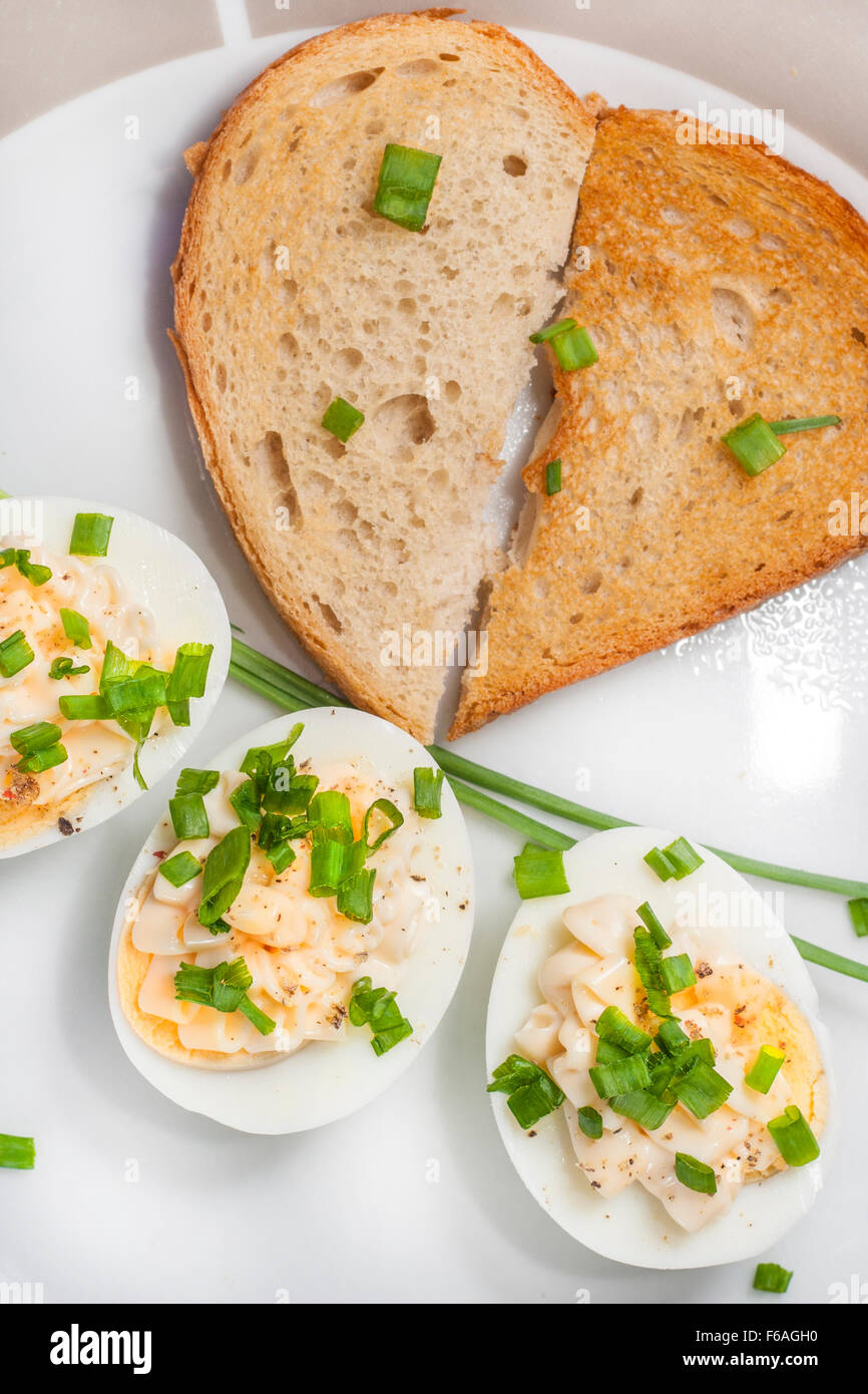 Boiled eggs with mayonnaise and sliced chive on plate and toasted bread arranged in heart shape