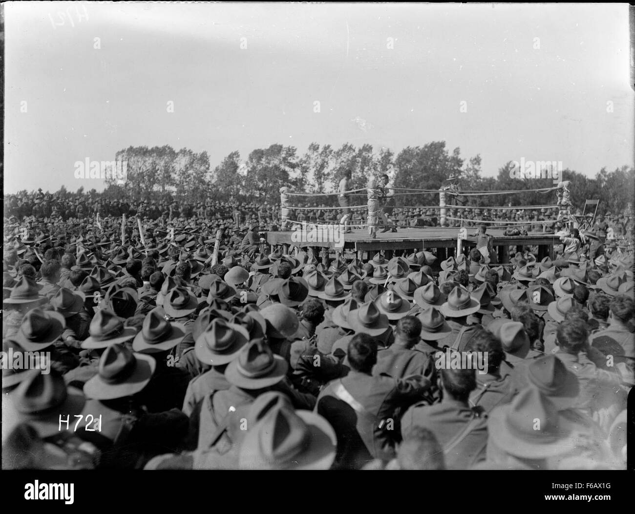 This historic photograph captures a crowd of soldiers gathered around to watch a boxing match, possibly in the early 20th century. The scene reflects the blend of military life and popular entertainment during wartime periods. Stock Photo