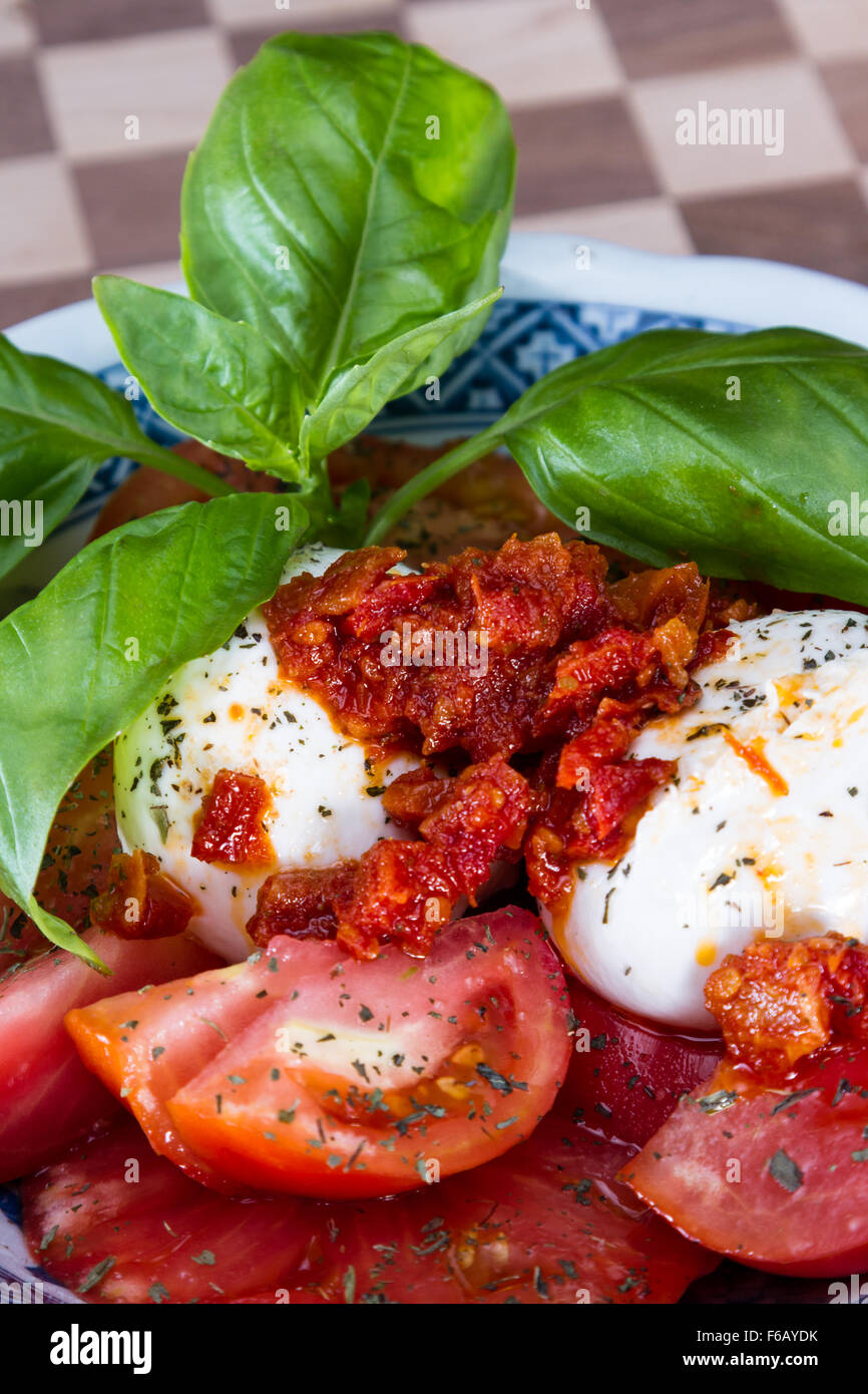 close up of a fresh mozzarella tomato salad with green basil leaves ...