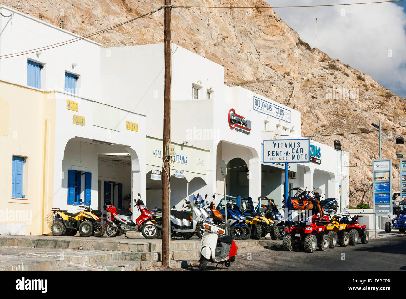 Santorini, Thira. Kamari. Vitanis rent-a-car and motorbike hire building.  Whitewashed with quad bikes in rows outside. Mountain backdrop Stock Photo  - Alamy
