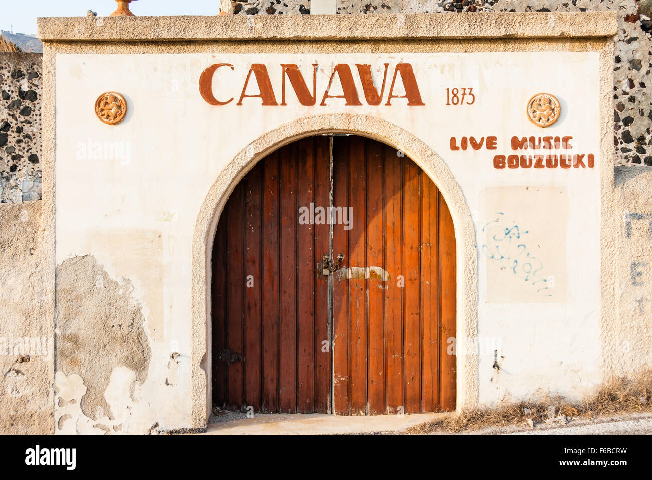 Santorini. Canava Roussos old winery, front main double wooden door, in old whitewashed wall with some broken rendering, early morning sunlight. Stock Photo