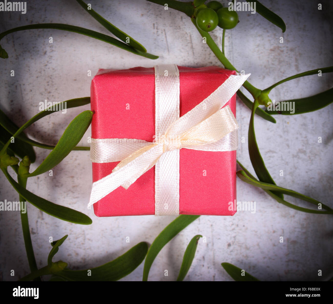 Wrapped red gift for Christmas or other celebration and branch of green mistletoe on old wooden background Stock Photo