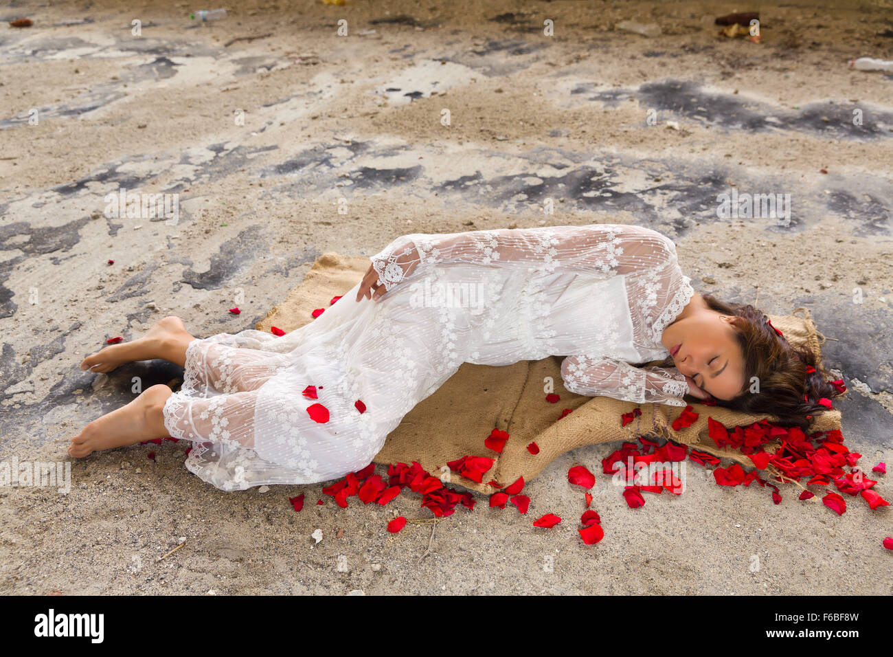 Young beautiful woman in antique lace gown sleeping in a derelict building with rose petals Stock Photo
