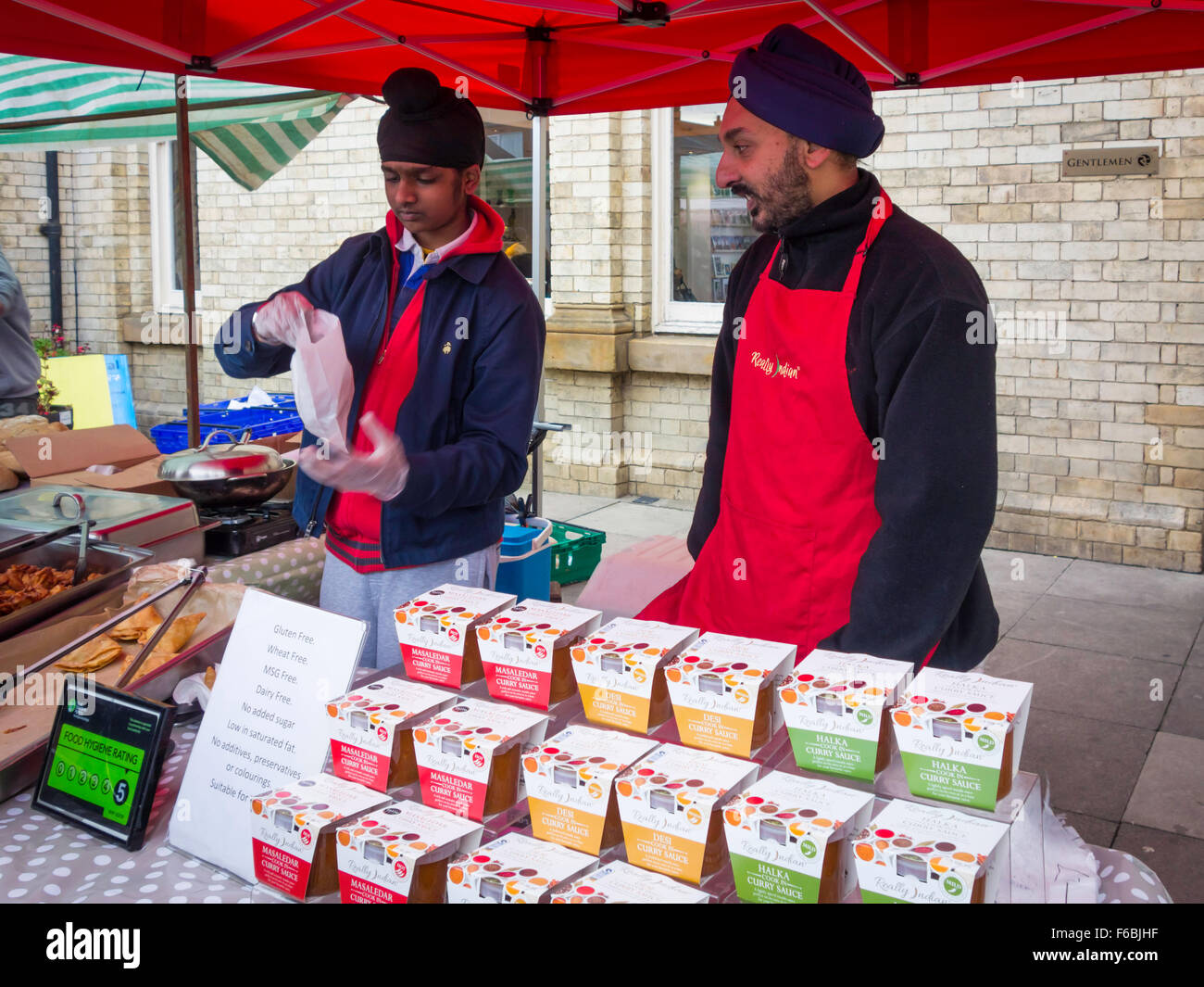 Two Sikh men stall holders at a UK farmer's market serving Curry Sauces and cooked 'Really Indian' brand food Stock Photo