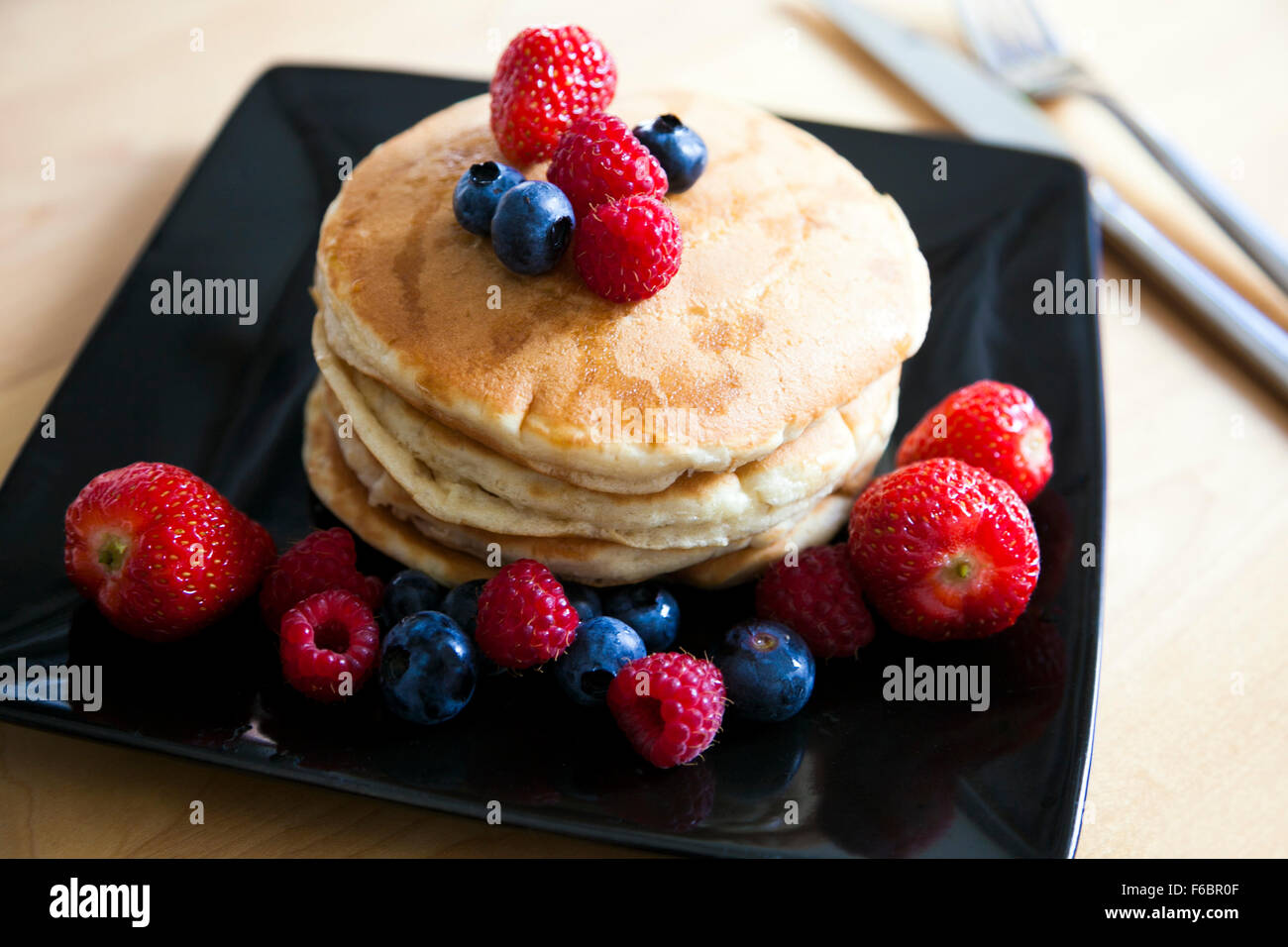 Fluffy pancakes with strawberries, blueberries, raspberries and maple syrup Stock Photo