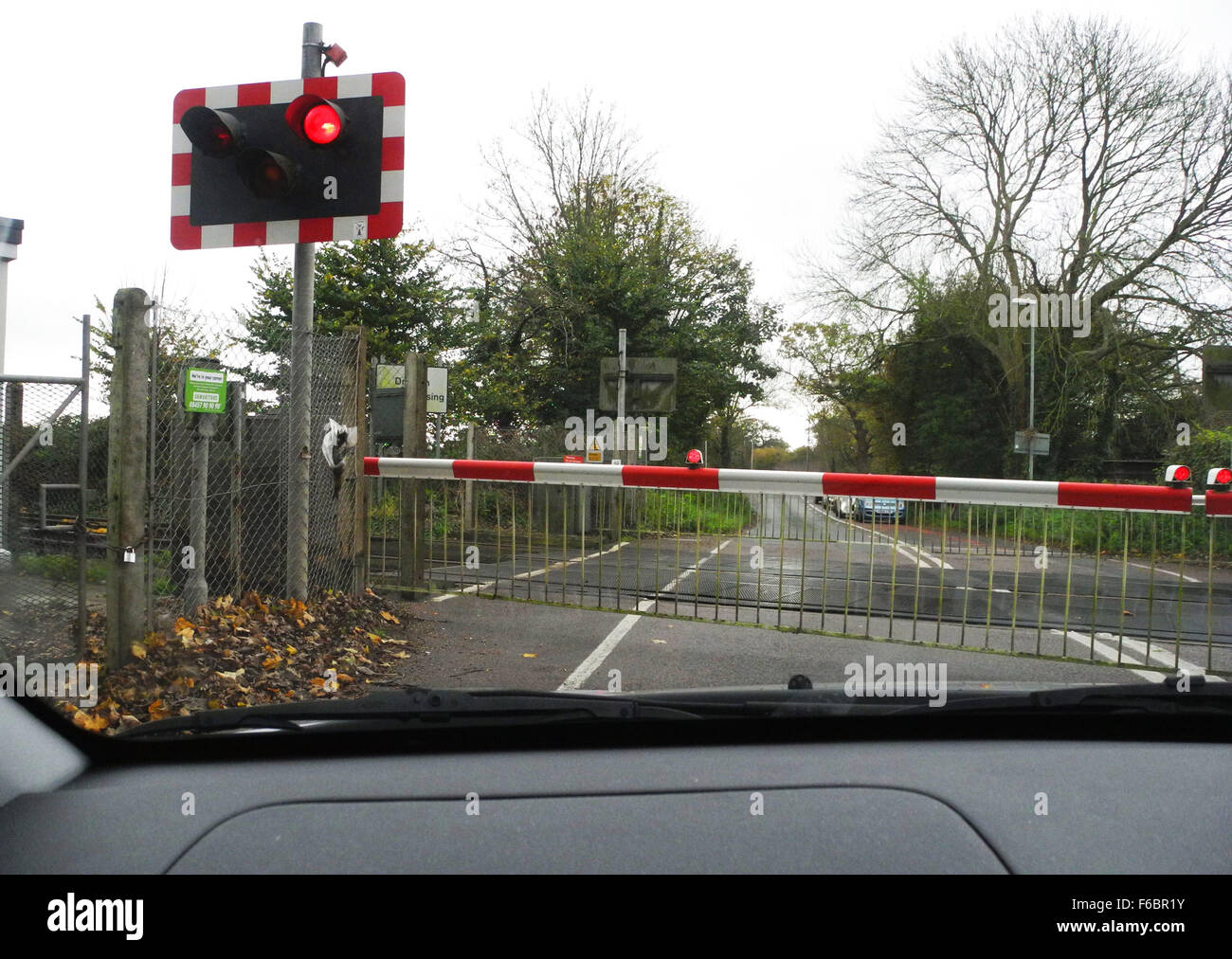 Railway level crossing with gates closed and train crossing. This one is at West Drayton near Chichester in West Sussex UK Stock Photo