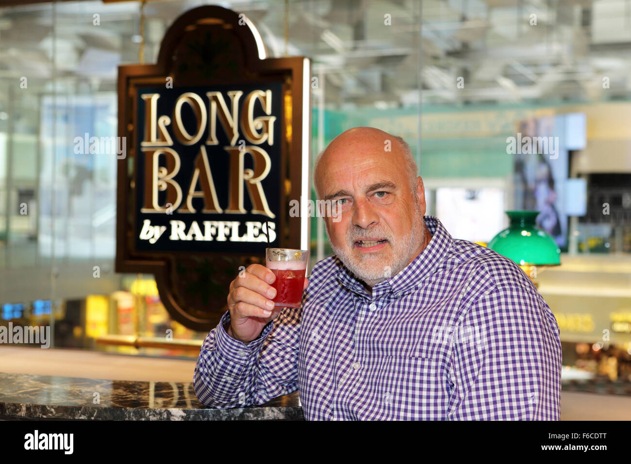 A man drinks a Singapore Sling cocktail at the Long Bar by Raffles at Changi International Airport in Singapore. Raffles is asso Stock Photo