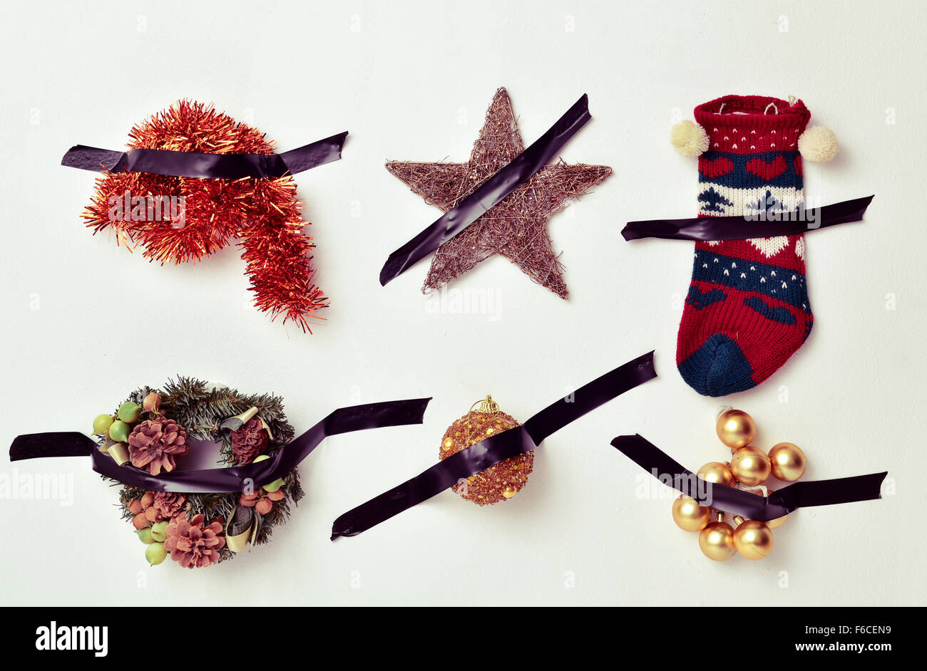 some different christmas ornaments, such as tinsel, a star, a stocking or baubles, attached to a white wall with black tape Stock Photo