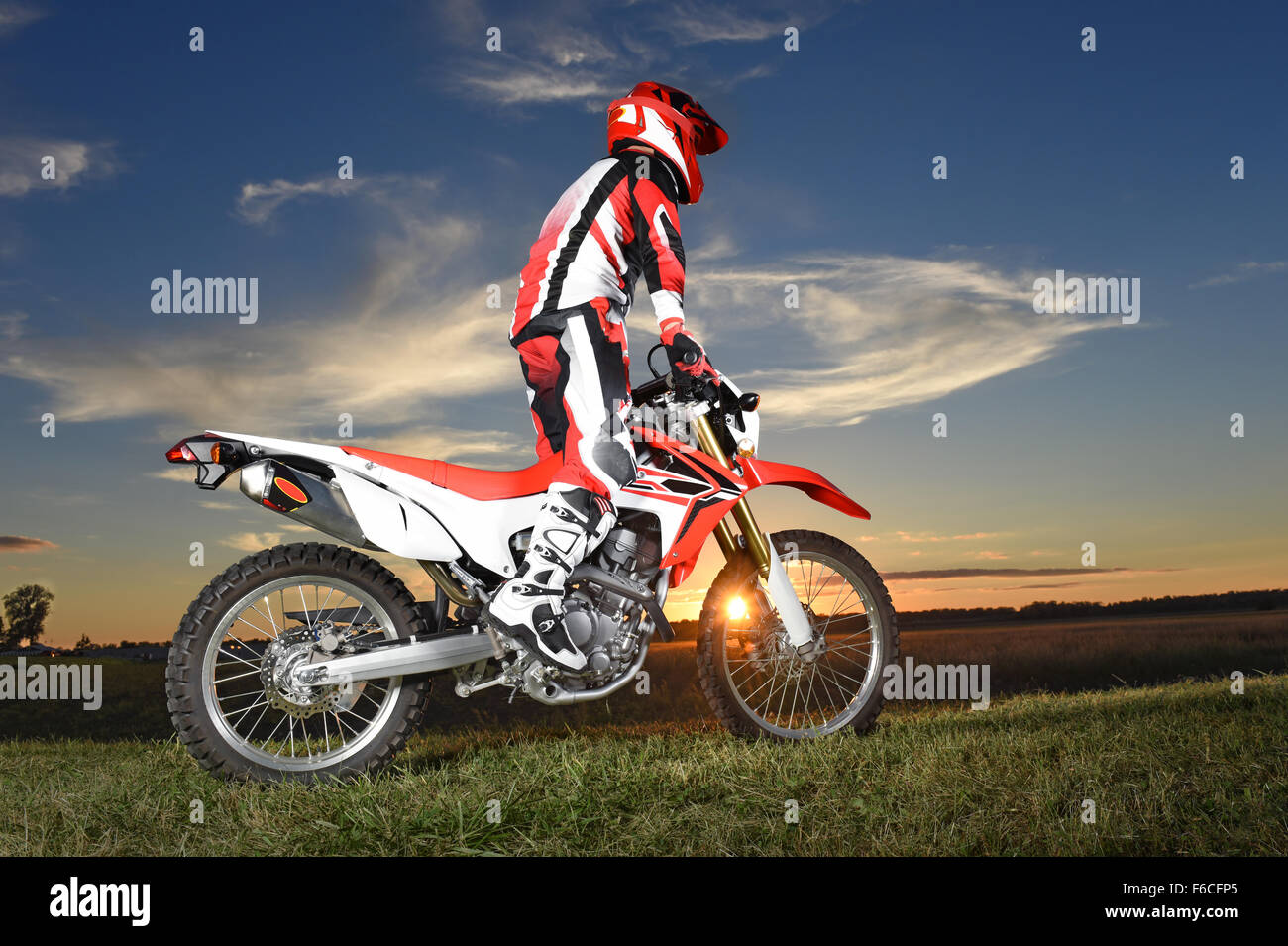 Motocross rider standing on motorcycle during sunset Stock Photo