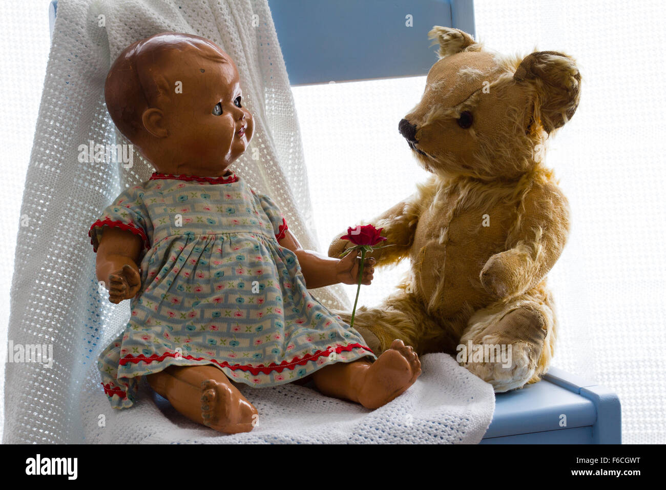 Story, concept. Antique teddy bear appears to accept a fresh red rose from a vintage ceramic doll. White background, copyspace Stock Photo