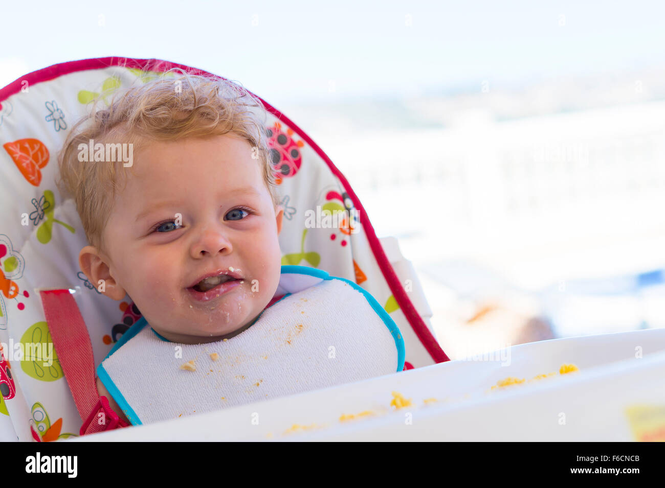 Gorgeous happy toddler eating food in high chair Stock Photo