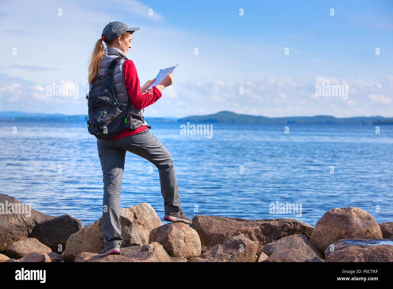 Young woman tourist with map and backpack standing on lake shore. Stock Photo