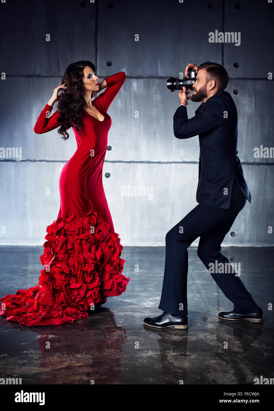 Young woman in red dress posing to man photographer. Elegant evening clothing. Stock Photo