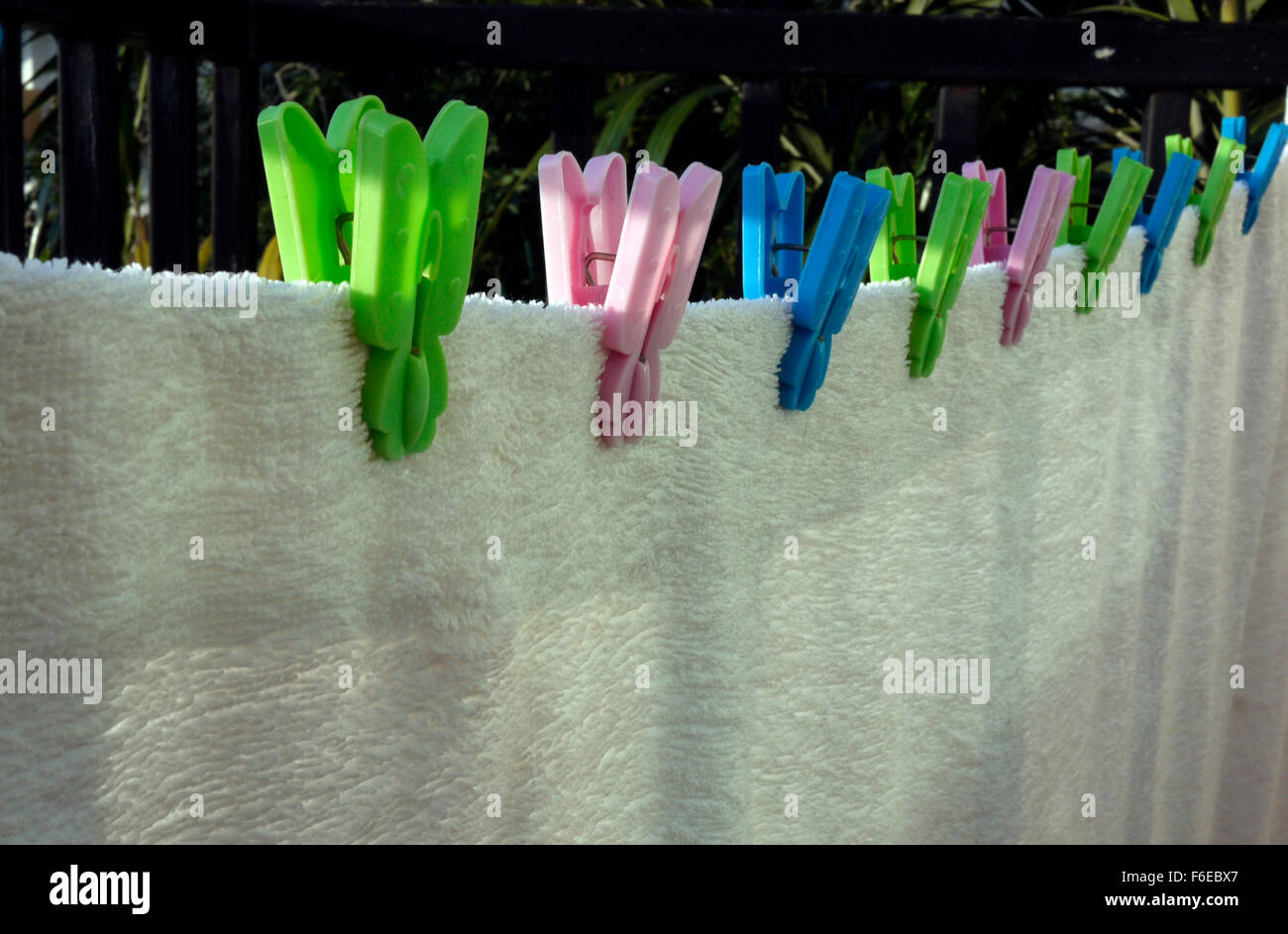 A white towel drying on a hotel balcony gripped with plastic clothes pegs Stock Photo