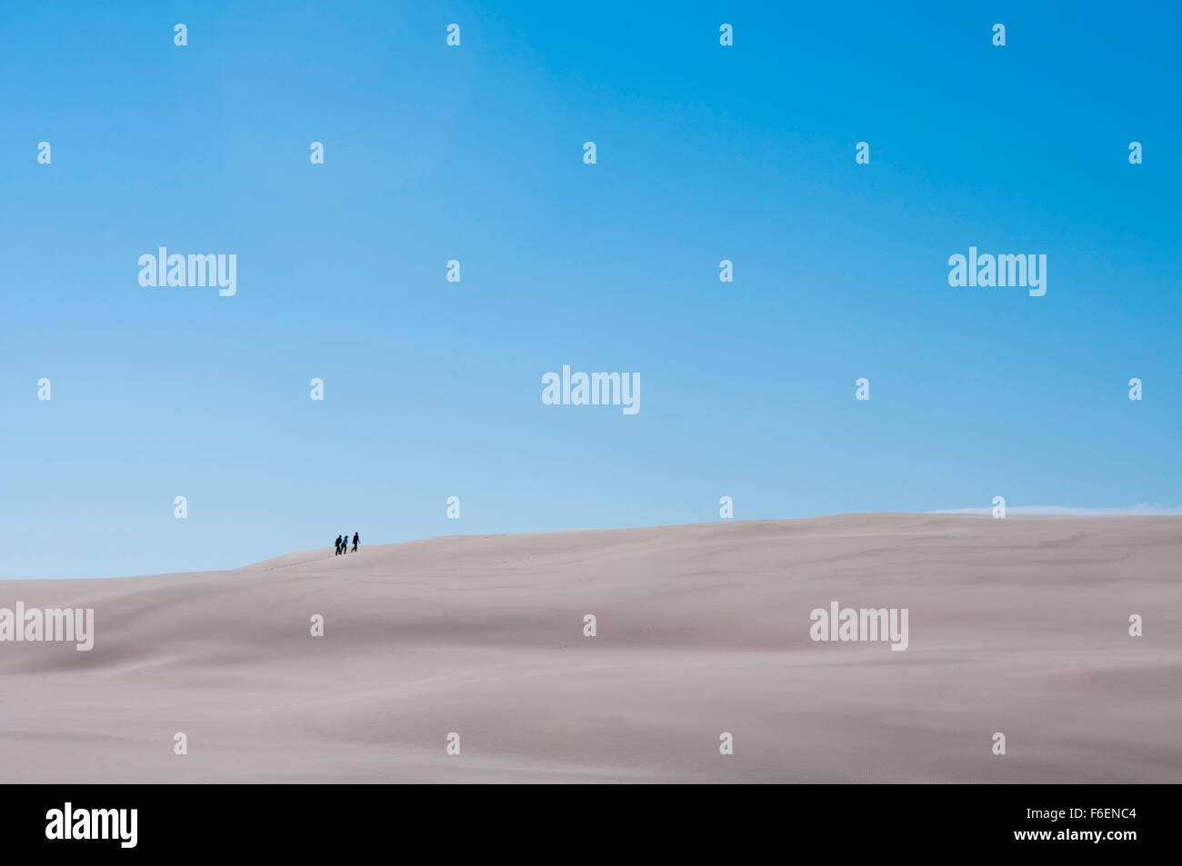 People in distance climbing white sand dune with clear sky on sunny day Stock Photo