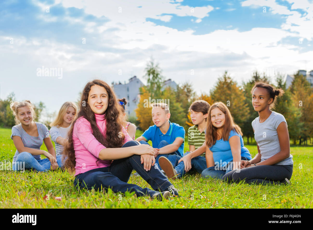 Happy group of friends sit together on meadow Stock Photo
