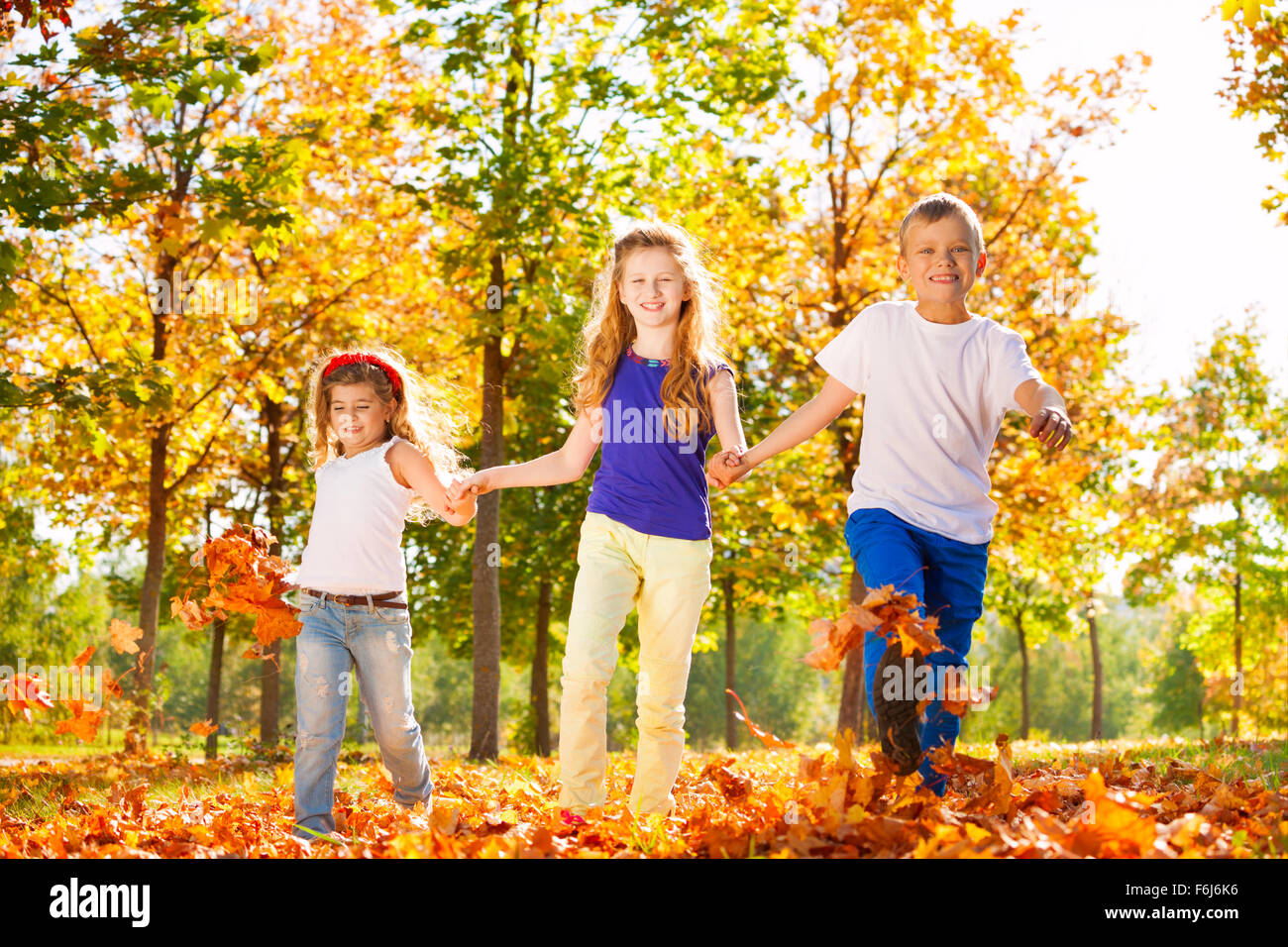 Three kids hold hands playing in the forest Stock Photo - Alamy