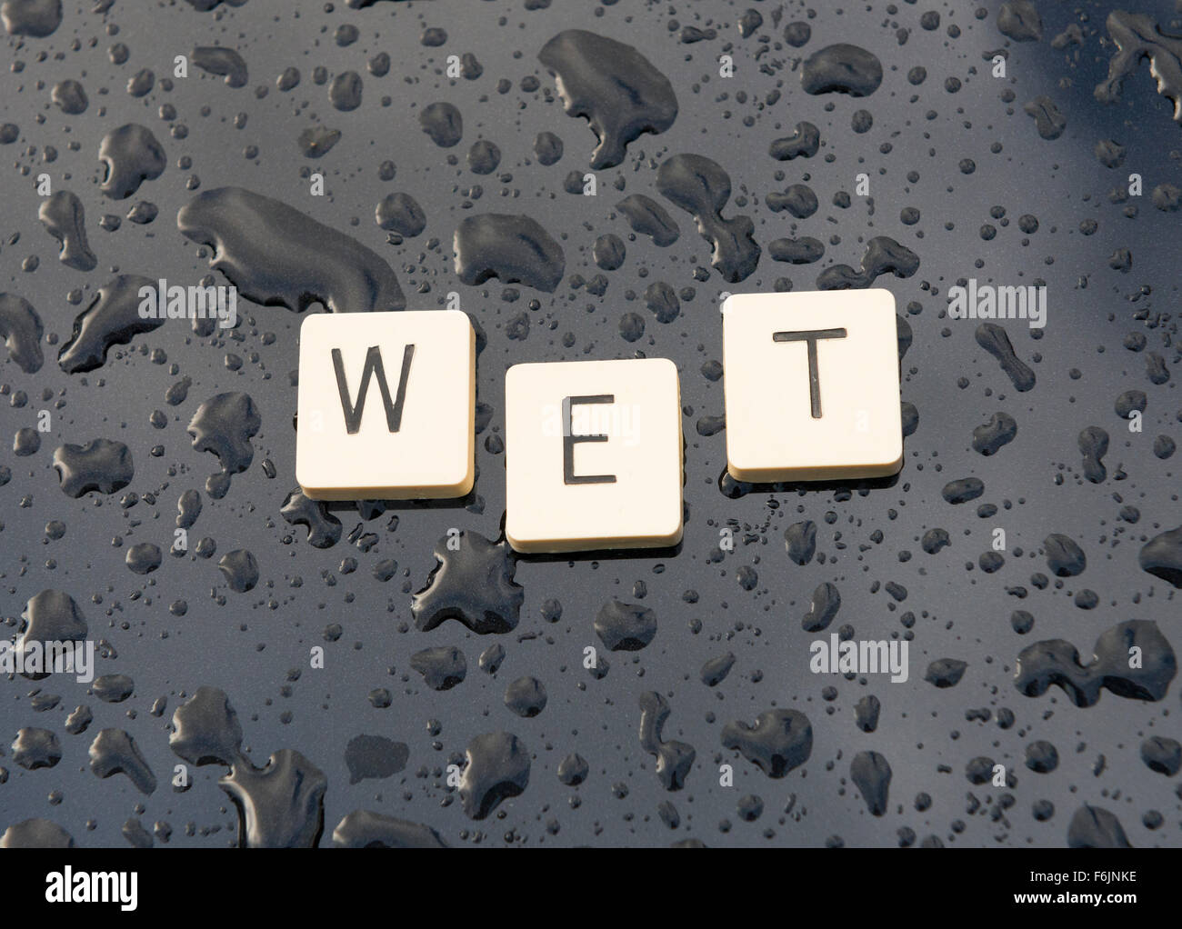 'Wet' spelt out on a rain soaked car bonnet. Stock Photo