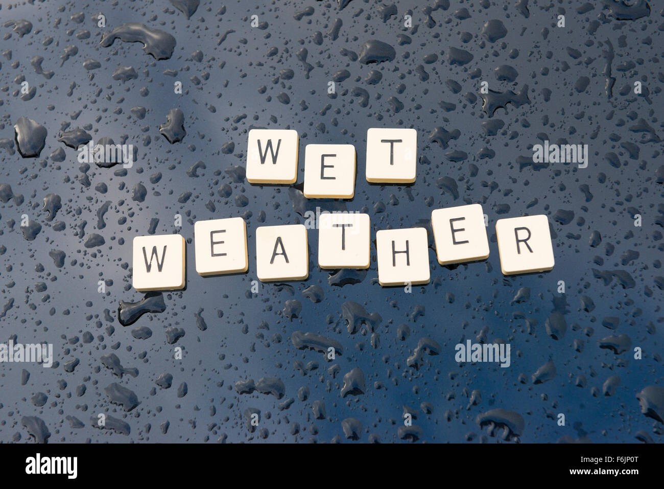 'Wet Weather' spelt out on a rain soaked car bonnet. Stock Photo