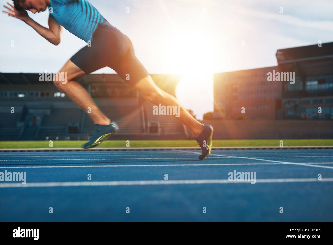 Shot of young male athlete launching off the start line in a race. Runner running on racetrack in athletics stadium. Stock Photo
