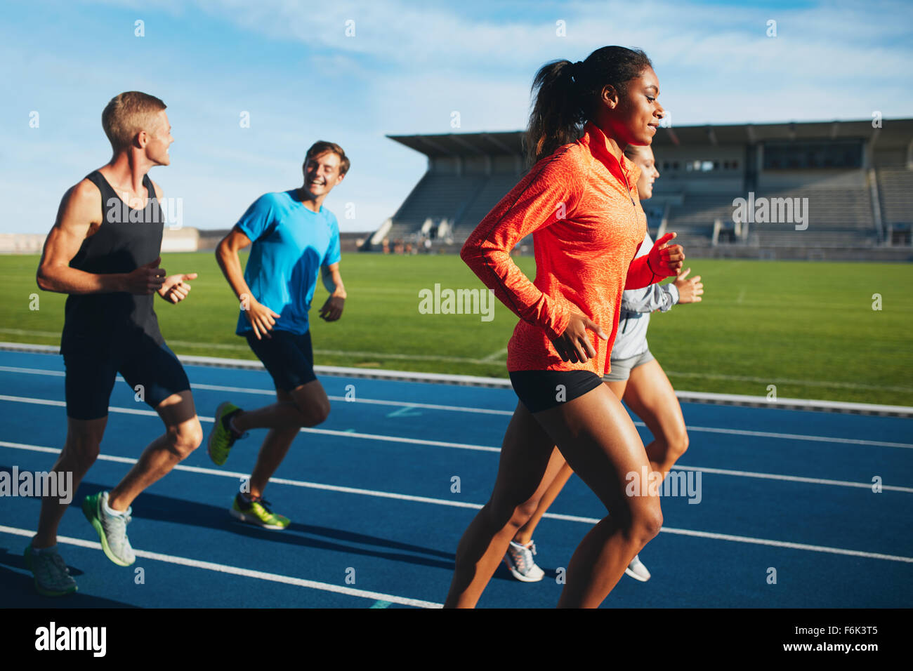 Fit men and women running on a race track. Multiracial athletes practicing on race track in stadium. Stock Photo
