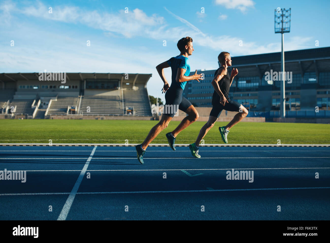 Two young men running on race track. Male professional athletes running
