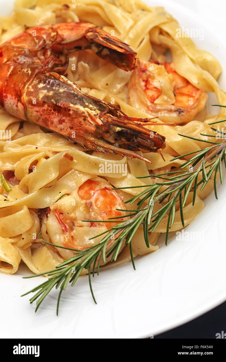 A dish of pasta with fried prawns on a white plate, garnished with rosemary. Stock Photo