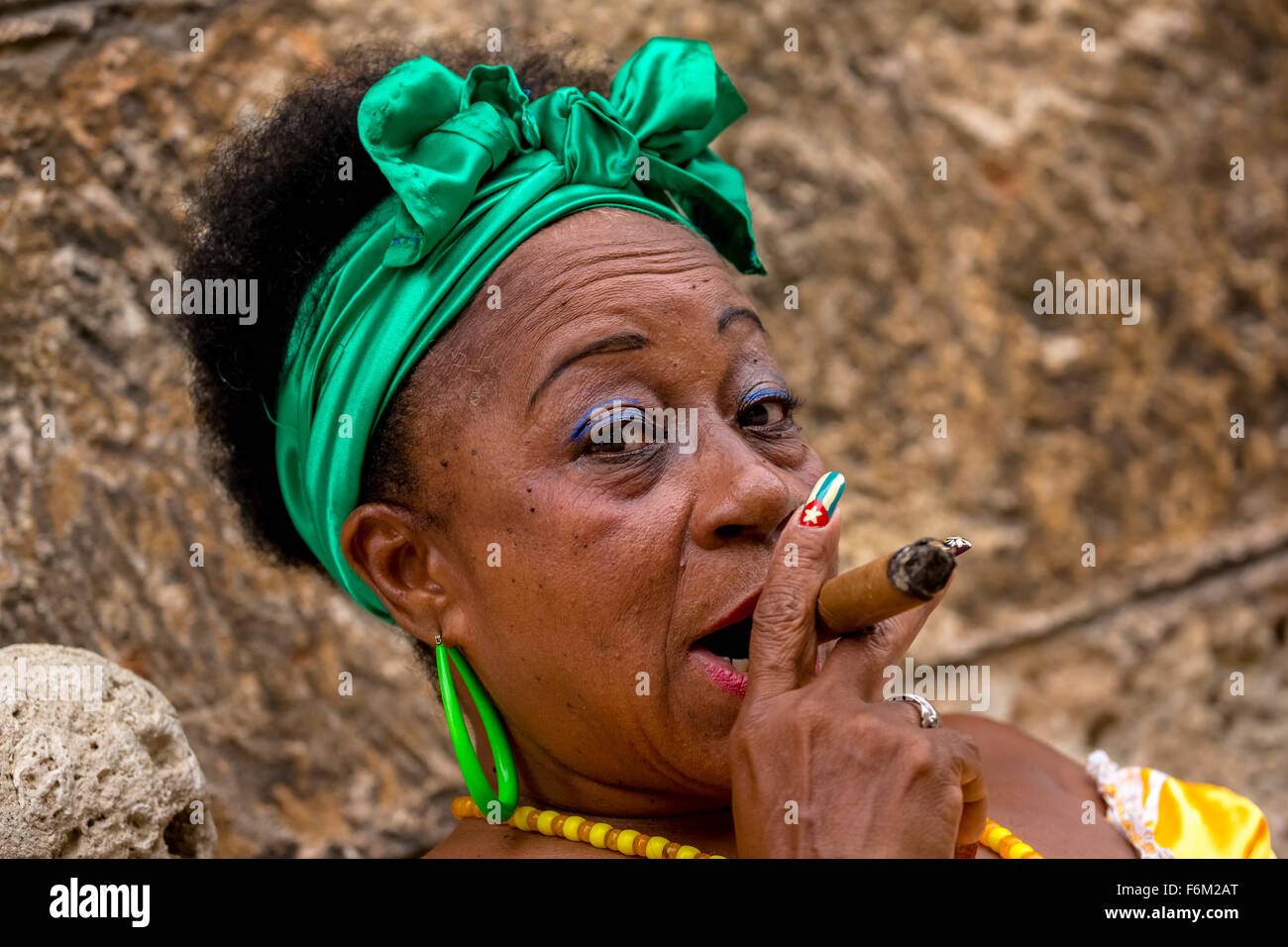 old heavily made Cuban woman with green hair bow smoking a Havana cigar, Cuban cigar with lacquered fingernails with Cuban Flag, Stock Photo