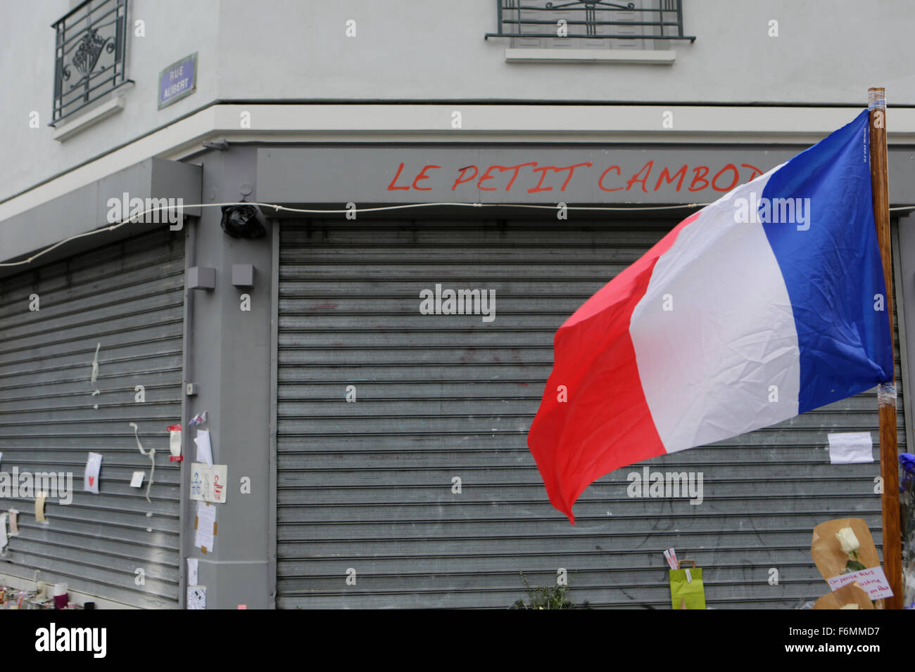 Paris, France. 17th Nov, 2015. A French flag waves at the memorial outside the restaurant Le Petit Cambodge for the people killed here during the Paris attacks. Parisians and tourists continue to visit the memorials for the people killed in the terrorists attacks in Paris, to lay down flowers and candles and to pay their respect. Over 130 people have been by terrorist from the Islamic State. Credit:  Michael Debets/Pacific Press/Alamy Live News Stock Photo