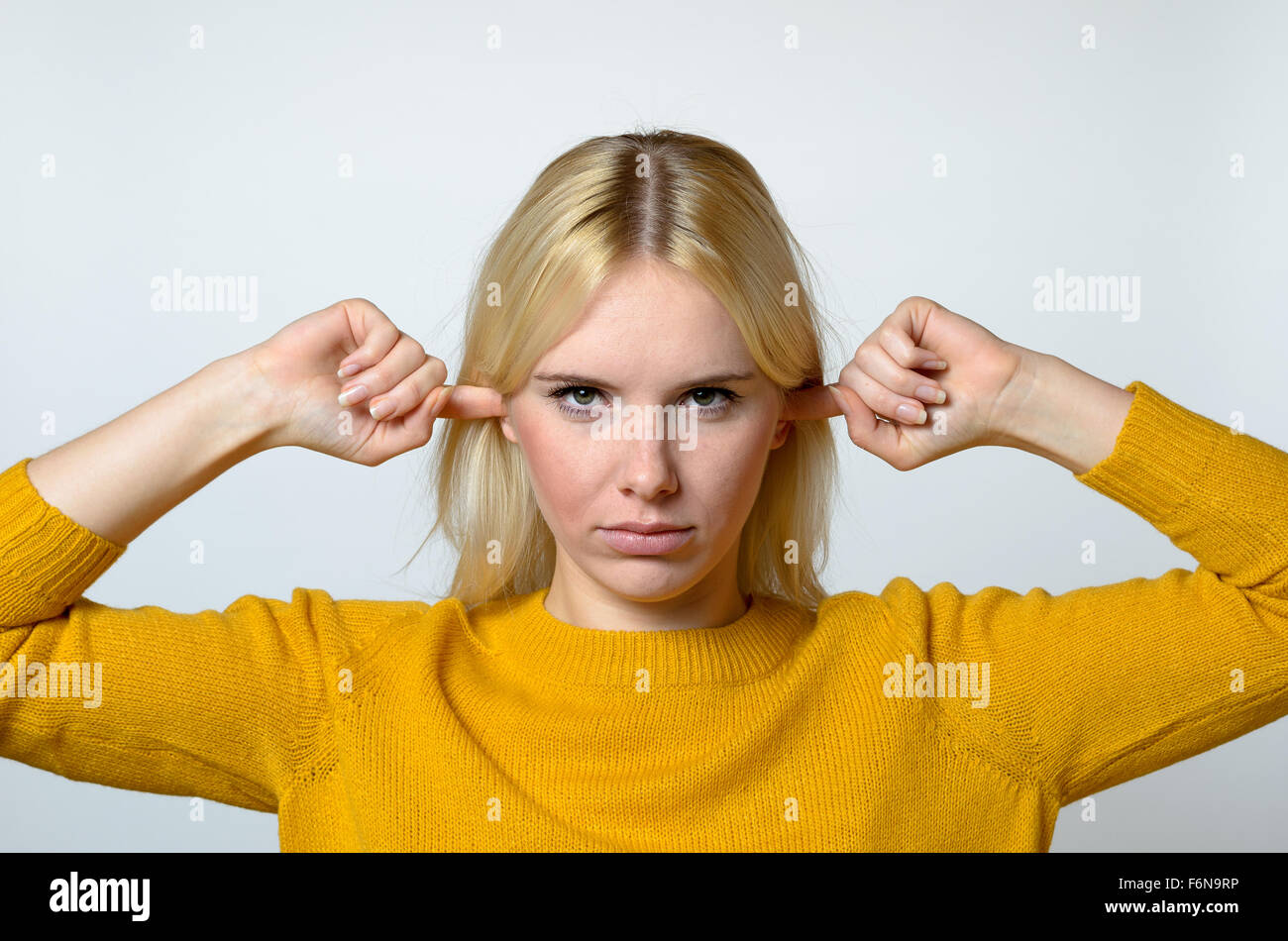 Close up Disgusted Young Woman Covering her Ears with Fingers, with open Eyes, Against Gray Background. Stock Photo