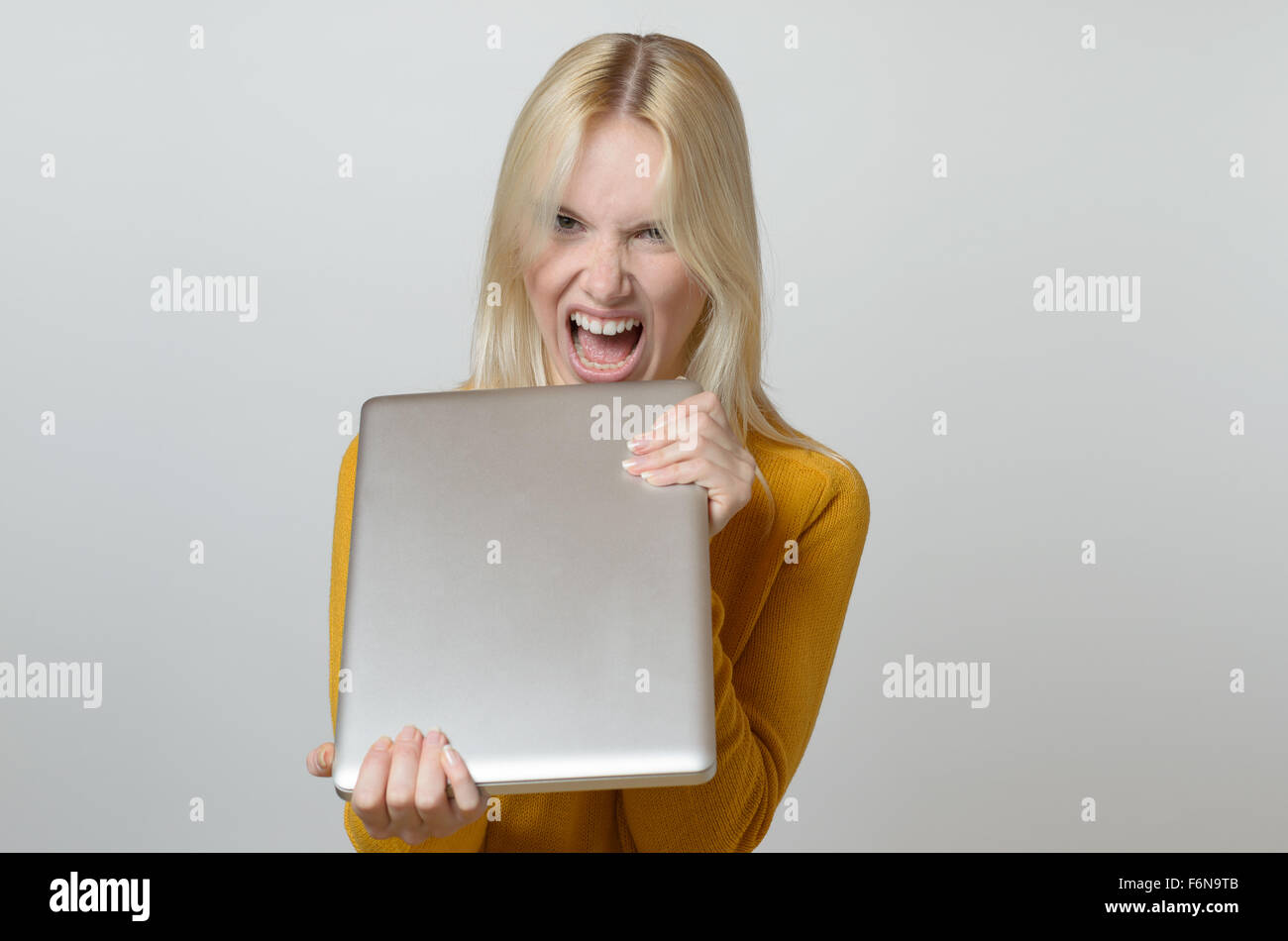 Blond Young Woman Showing Angry Face at the Camera While Holding her Laptop Computer Against White Background. Stock Photo
