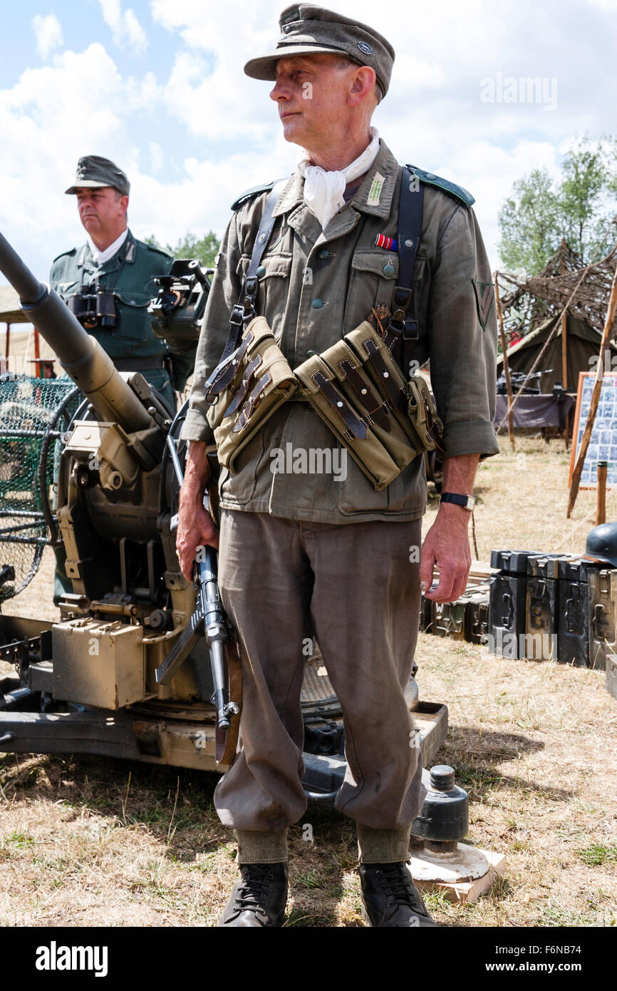 WW2 re-enactment. Wehrmacht German officer standing in combat uniform, wearing M38/40 ammo pouches, and M43 woollen cap. Holding sub machine gun. Stock Photo