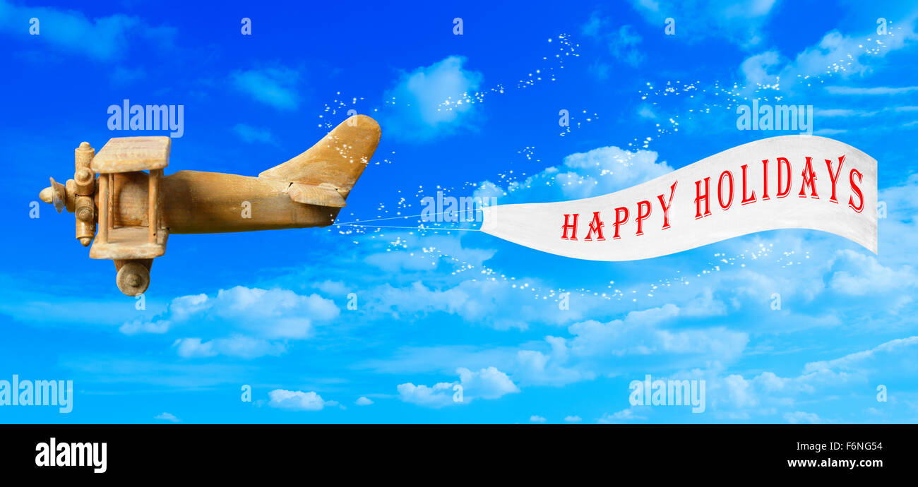 Vintage wooden toy plane flying in blue sky pulling a Happy Holidays banner Stock Photo