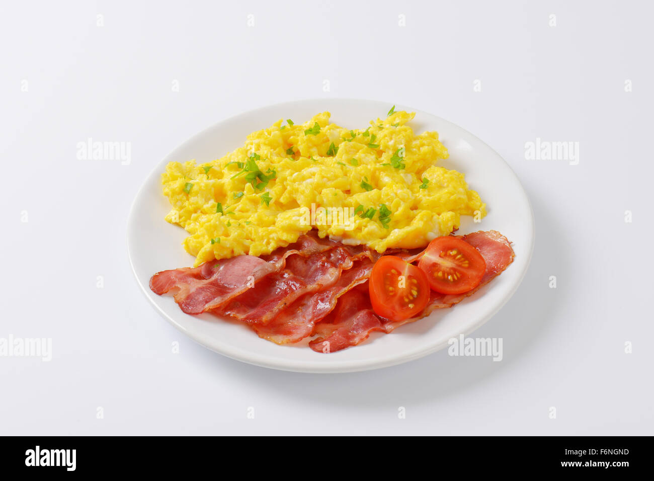 plate of scrambled eggs and slices of fried bacon on white background ...