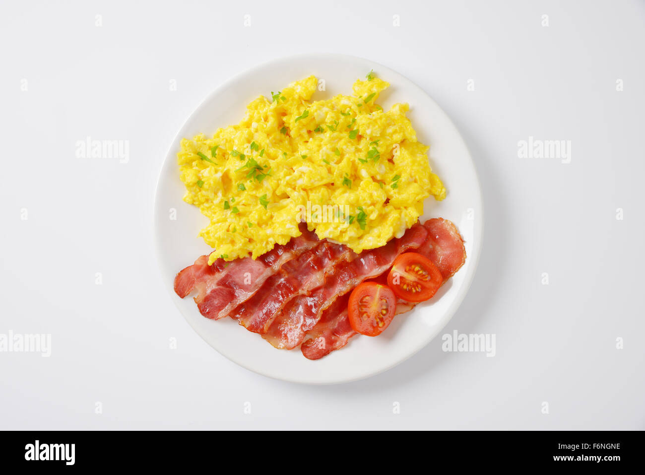 plate of scrambled eggs and slices of fried bacon on white background ...