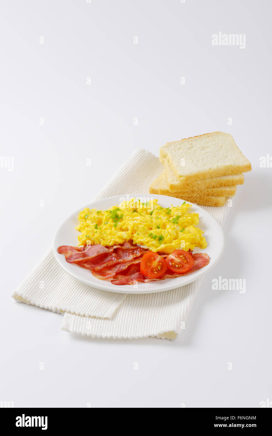 plate of scrambled eggs and fried bacon and slices of bread on white ...