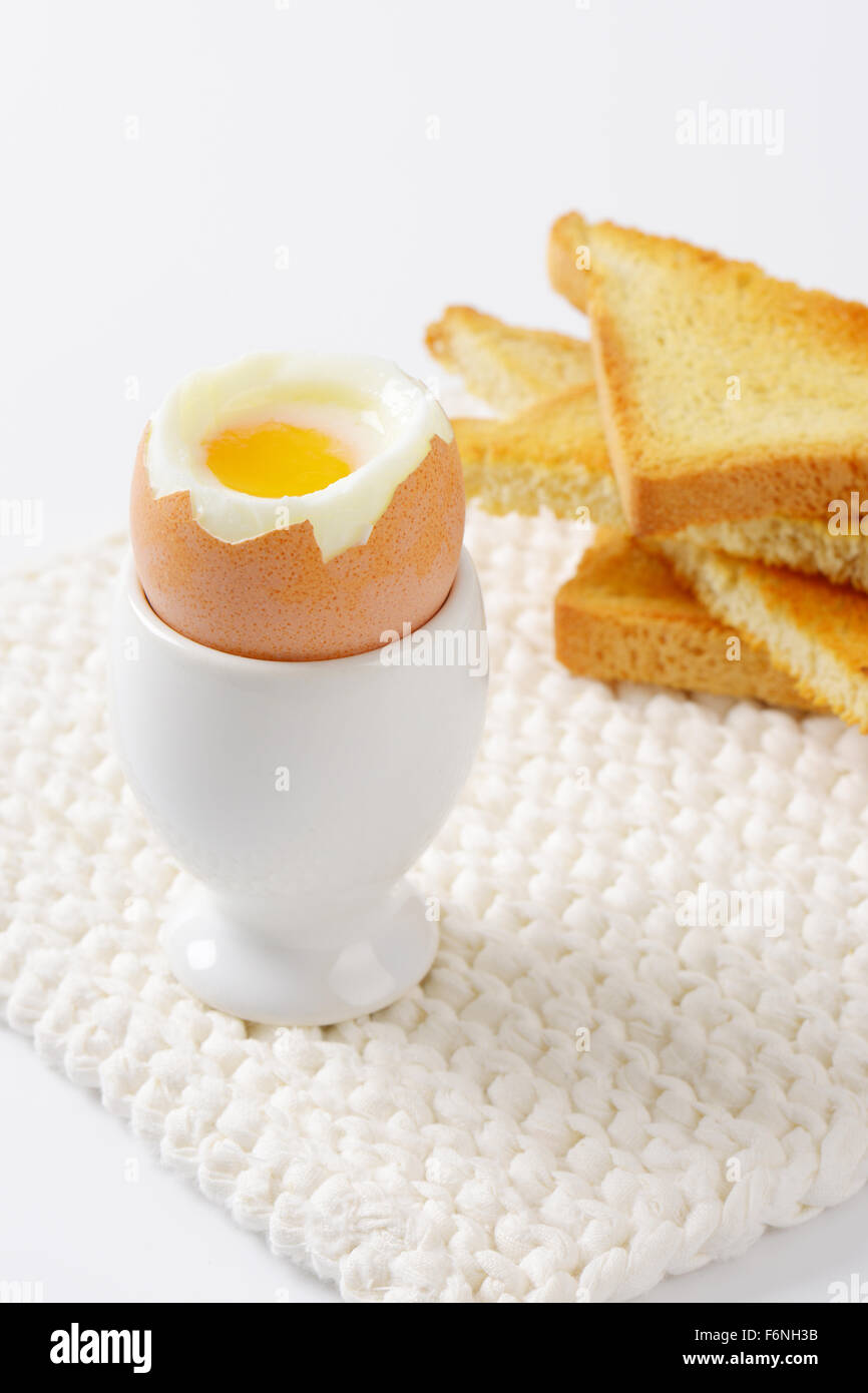 close up of soft boiled egg in egg cup and crispy toasts on white table mat Stock Photo