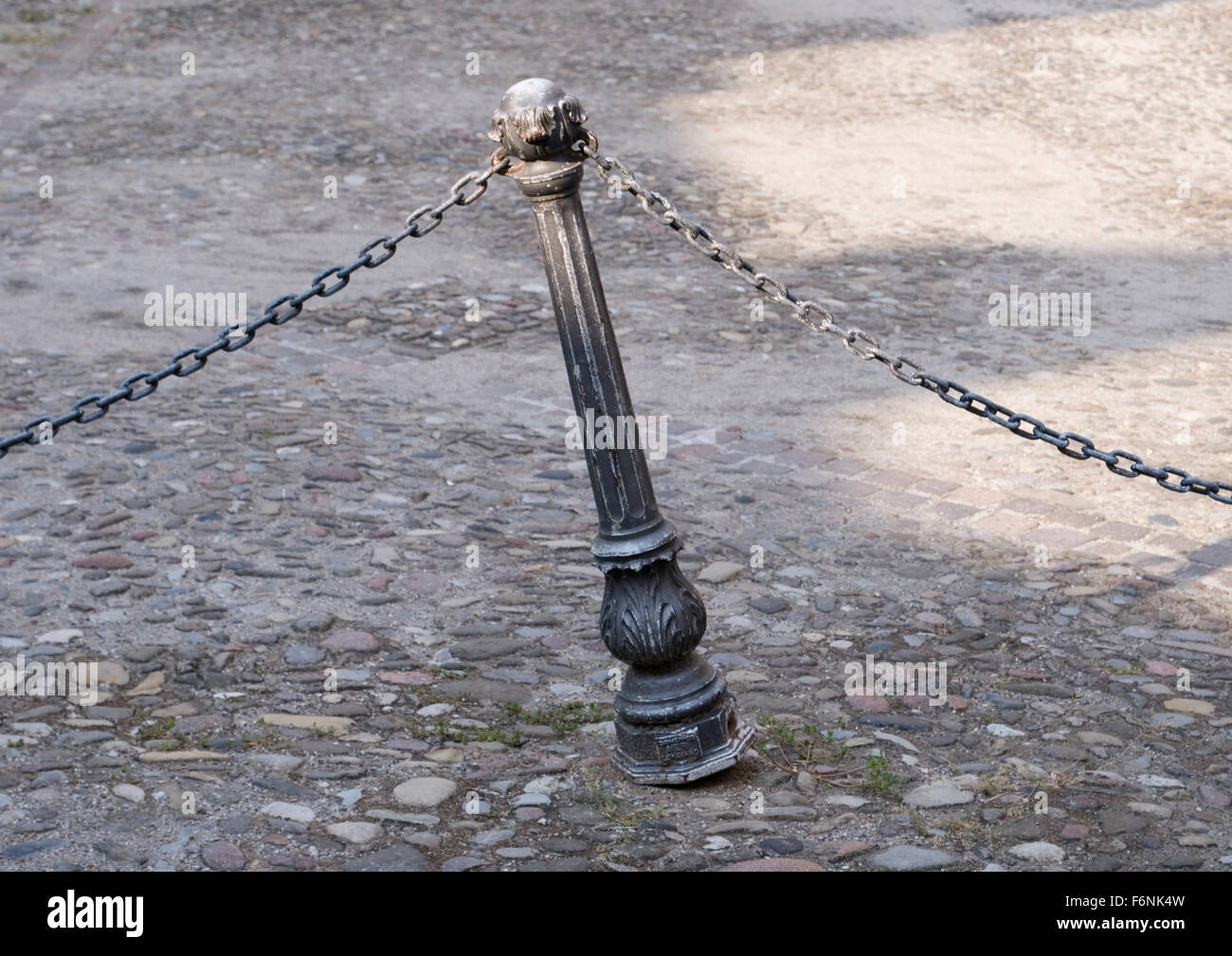 antique leaning metal pole with chain on a street in Italy Stock Photo