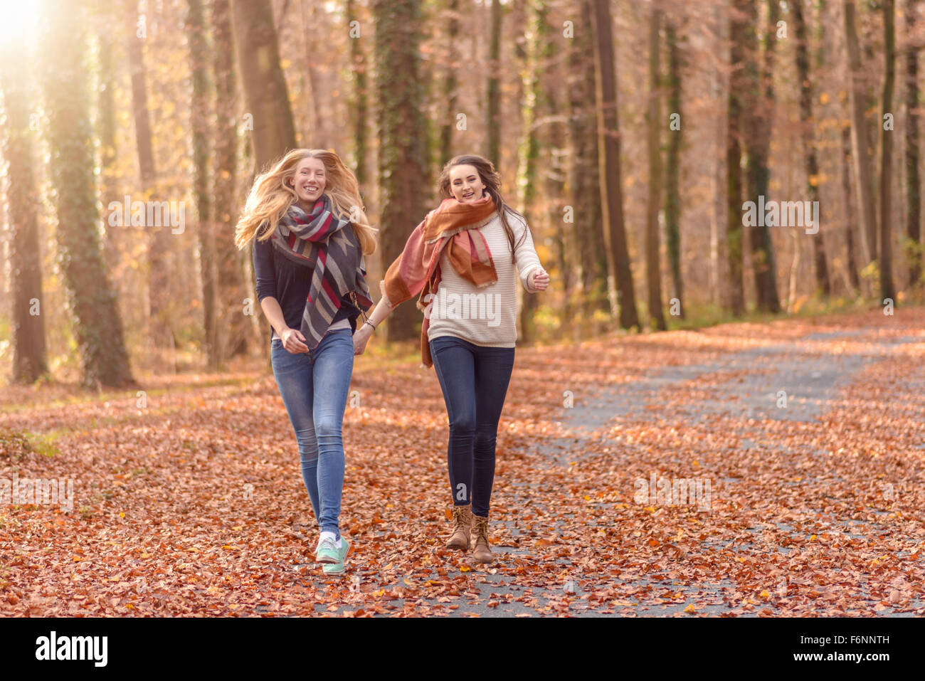 Two joyful women running hand in hand through a wooded autumn park with ...
