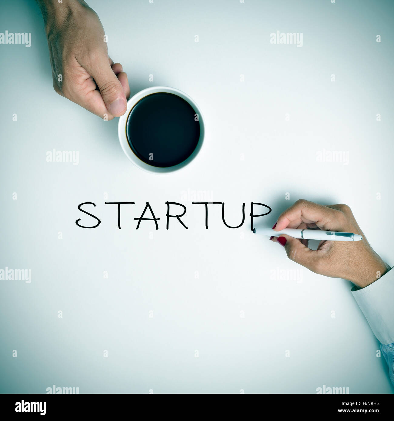 high-angle shot of a young man with a cup of coffee and a young woman writing the text startup with a pen Stock Photo