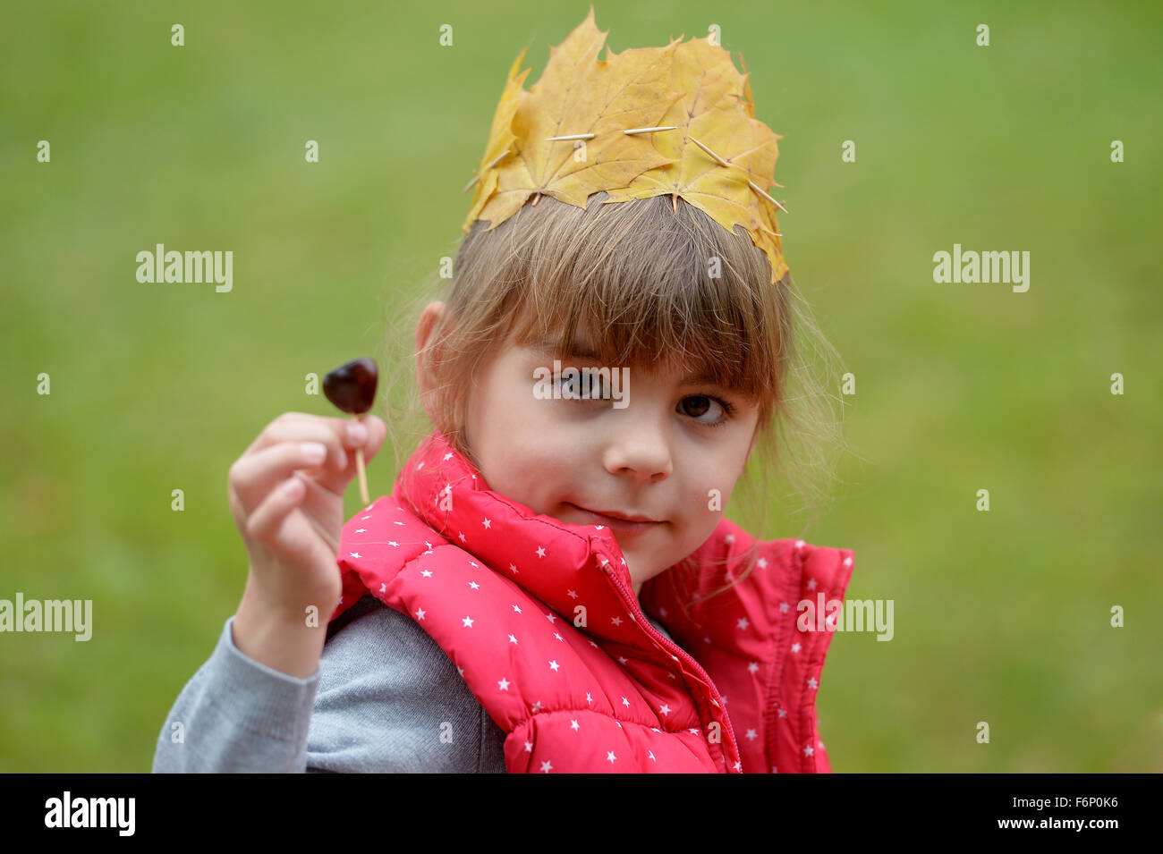 A girl wearing a crown of leaves is showing a chestnut with a match. Stock Photo