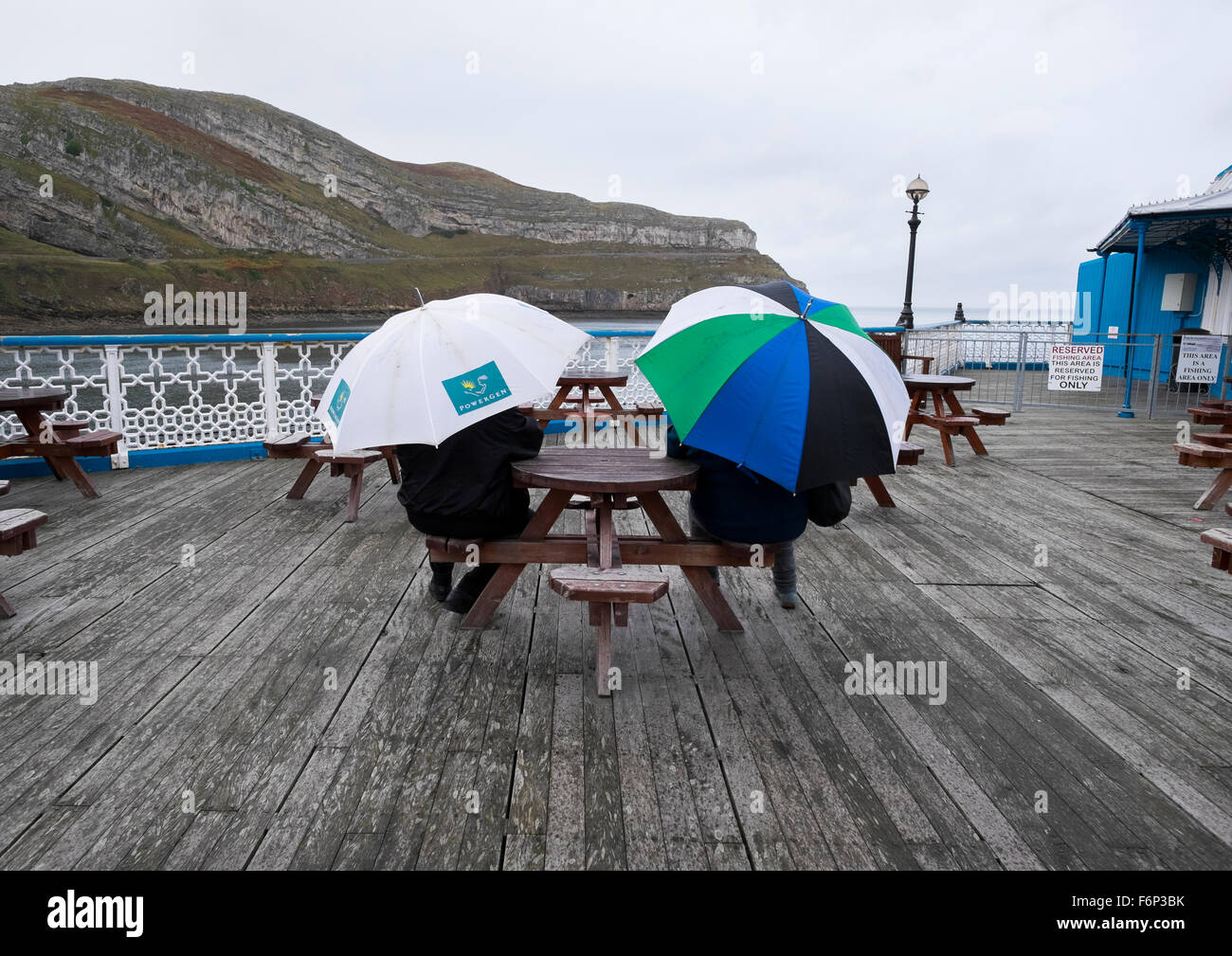 Two people shelter under umbrellas on Llandudno Pier, Conwy, Wales, UK Stock Photo