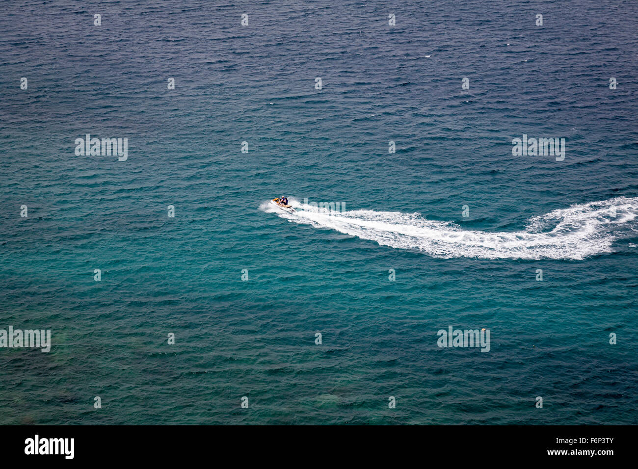 Viewed from above, a speed boat creates a dramatic white wash across a turquoise tropical sea. Stock Photo