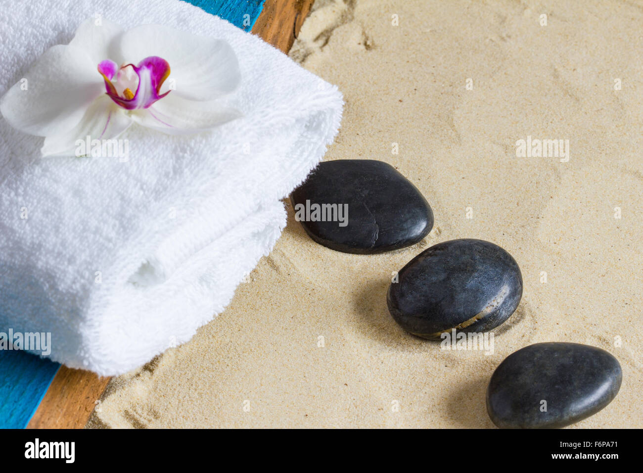 Black basalt stones, white towel, orchid flower, aqua painted wood on a sand background.  Closeup, copyspace, selective focus Stock Photo